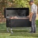 A man standing in front of a Backyard Pro smoker grill with meat on it.