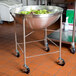 A Vollrath stainless steel mobile mixing bowl stand with a large metal bowl of salad inside.