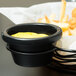 A Tablecraft black metal basket with yellow sauce in a ramekin next to french fries.