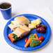 A blue Creative Converting round paper plate with a sandwich, carrots, and a cup of coffee.