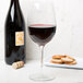 A Reserve by Libbey wine glass filled with red wine next to a bottle of crackers.