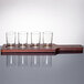 A mahogany Libbey flight paddle holding four straight sided tasting glasses.