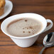 A 10 Strawberry Street white bone china cappuccino cup filled with brown liquid on a saucer with a spoon and muffin.