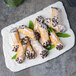A 10 Strawberry Street rectangular porcelain platter with cannoli topped with chocolate chips on a table.