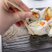 A hand holding chopsticks to a rectangular stoneware slab with sushi.