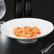 A white porcelain bowl filled with spaghetti and sauce on a table.