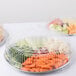 A Durable Packaging round foil catering tray containing plastic containers of vegetables and fruit.