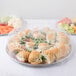 A Durable Packaging round foil catering tray with a variety of food in plastic containers.