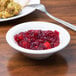 A Tuxton Nevada eggshell narrow rim china bowl filled with cranberry sauce on a table with a plate of food and a spoon.