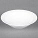An Arcoroc white porcelain bowl with a rim on a gray surface.