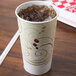 A Solo paper cold cup with a straw in it filled with ice tea on a wood surface.