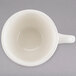 A white Tuxton espresso cup with a handle on a gray surface.
