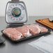 A CKF black foam meat tray with raw meat on a counter.