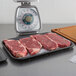 A black CKF foam meat tray holding raw steaks on a kitchen counter.