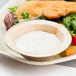 A plate of fish and salad with a bowl of white sauce served in an EcoChoice palm leaf bowl.