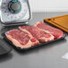 A black CKF foam meat tray filled with raw meat on a counter.