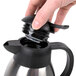 A hand opening a black plastic lid on a coffee server.