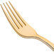 A close up of a Fineline gold plastic fork with a white background.