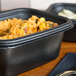 A black Genpak Smart-Set Pro rectangular microwaveable container with food in it.