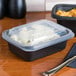 A black Genpak rectangular plastic container with food in it on a table.