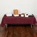 A table with Creative Converting Burgundy Tissue/Poly Table Cover on it with food.