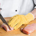 A person cutting meat on a cutting board with a San Jamar yellow cut resistant glove.