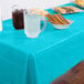 A wooden table with a Bermuda Blue Creative Converting plastic table cover with drinks and snacks on it.