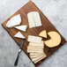A Tablecraft acacia wood rectangular serving board with cheese and crackers on a wooden surface.