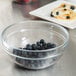 An Arcoroc stackable glass bowl filled with blueberries on a table.