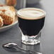 A Libbey Gibraltar espresso glass filled with dark liquid and foam with a spoon on the side.