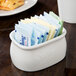 A white CAC porcelain sugar packet holder on a table with sugar packets inside.