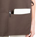 A woman wearing a brown Intedge cobbler apron with a pocket holding a pen and notebook.