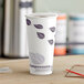 A close-up of a white EcoChoice paper hot cup with purple leaf design on a table.