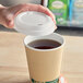 A hand placing a white EcoChoice compostable lid on a paper cup of tea.