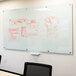 A white Aarco glass markerboard with red marker drawings on it.