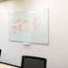 A white Aarco pure glass markerboard with red marker drawings on it.