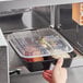 A hand reaching into a black Choice rectangular microwavable container with food in it.