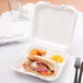 A sandwich with meat and vegetables in a Genpak white foam 3-compartment takeout container.