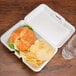 A sandwich and potato chips in a white styrofoam container.
