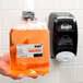 A hand holding a plastic bottle of GOJO orange liquid soap.