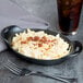 A Lodge mini cast iron casserole dish filled with macaroni and cheese on a table with a glass of brown liquid with ice.