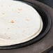 A tortilla on a Lodge cast iron fajita skillet on a black plate.