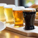 A tray of Libbey Mini Pub Beer Tasting Glasses on a wooden board with a couple of glasses of beer.