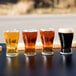 A row of four Libbey Mini Pub Beer Tasting Glasses filled with beer on a table.