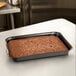 A Solut black quarter size sheet pan with a brownie in it on a metal table.