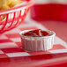 A small container of ketchup on a red and white checkered tablecloth with french fries.