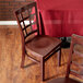 A Lancaster Table & Seating mahogany wood chair with a mahogany wood seat next to a table with a red tablecloth.