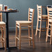 A group of Lancaster Table & Seating wooden bar stools with ladder backs and natural wood seats stacked together.