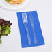 A fork and knife on a cobalt blue Creative Converting guest towel next to a plate of salad.