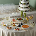 A table with Visions white plastic plates with gold lattice design and food and glasses on it.
